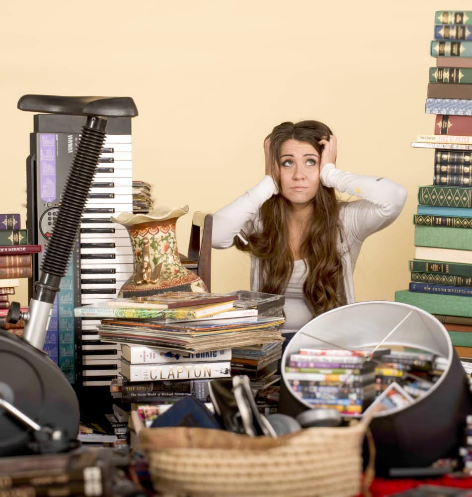 Woman overwhelmed by clutter, surrounded by books, electronics and household items before a move