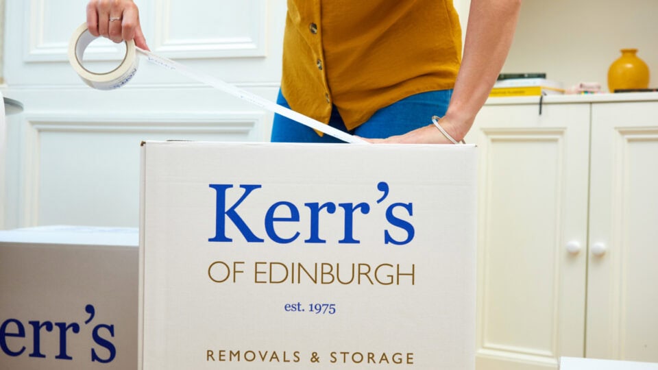 Woman sealing a Kerr’s of Edinburgh storage box during home packing for self-storage